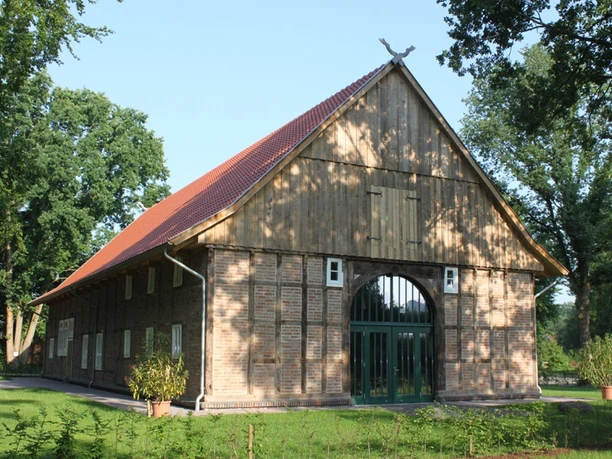 Historisches Fachwerkhaus mit Backsteinmauern und rotem Satteldach, von Bäumen umgeben.