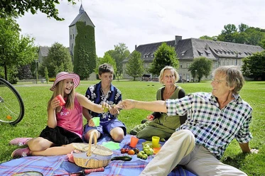 Picknick im Schlosspark Brakel-Gehrden Eine Familie genießt bei Sonnenschein ein Picknick auf einer Wiese vor einem historischen Schloss.