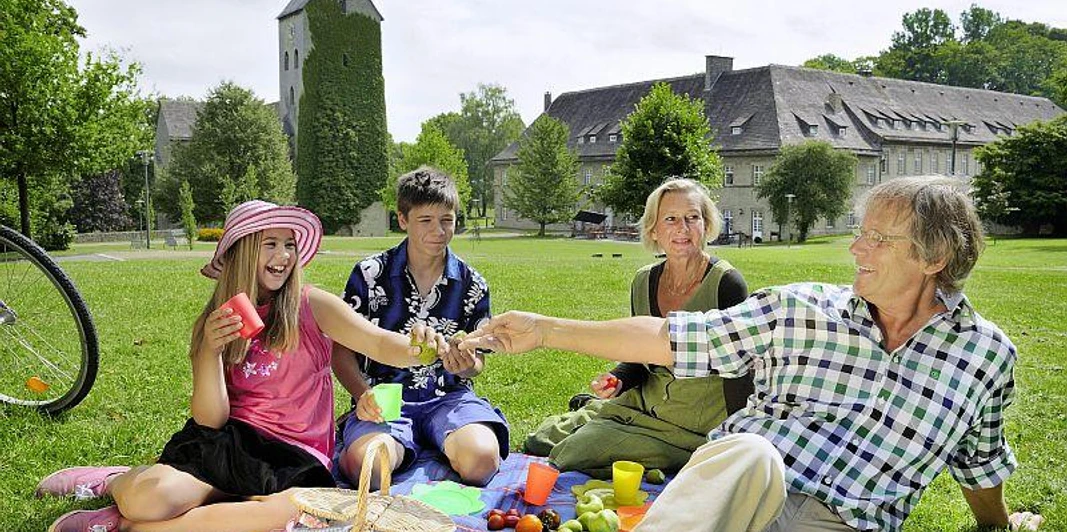 Picknick im Schlosspark Brakel-Gehrden Eine Familie genießt bei Sonnenschein ein Picknick auf einer Wiese vor einem historischen Schloss.