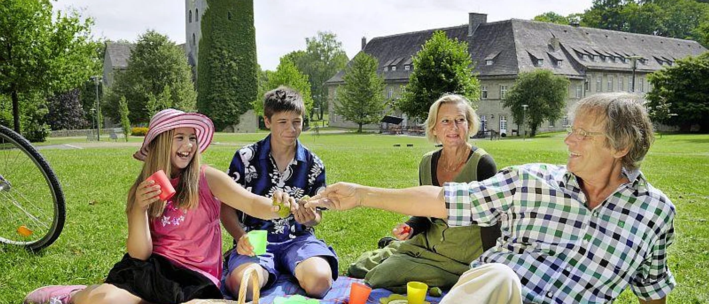 Picknick im Schlosspark Brakel-Gehrden Eine Familie genießt bei Sonnenschein ein Picknick auf einer Wiese vor einem historischen Schloss.