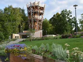 Holzturm des Baumwipfelpfads Bad Iburg, umgeben von gepflegten Gärten und üppiger Vegetation.