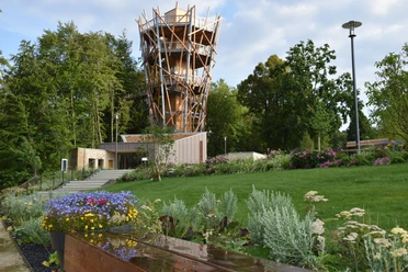 Baumwipfelpfad Bad Iburg Holzturm des Baumwipfelpfads Bad Iburg, umgeben von gepflegten Gärten und üppiger Vegetation.