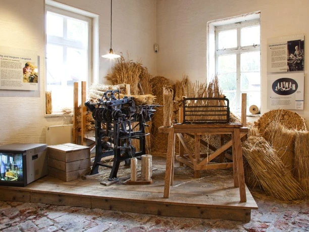 Glashütte Gernheim: Korbflechterei Historische Werkstatt mit traditionellen Werkzeugen für Korbflechterei, umgeben von getrocknetem Stroh.