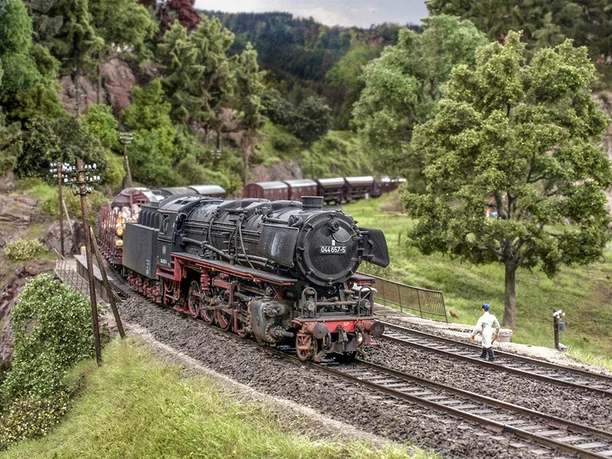 Dampflokomotive der Baureihe 44 fährt durch eine modellierte Landschaft mit Bäumen und Hügeln.