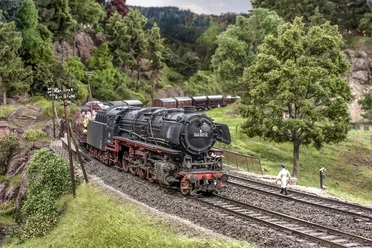 Modellbundesbahn Dampflokomotive Baureihe 44 Dampflokomotive der Baureihe 44 fährt durch eine modellierte Landschaft mit Bäumen und Hügeln.