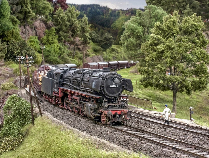 Modellbundesbahn Dampflokomotive Baureihe 44 Dampflokomotive der Baureihe 44 fährt durch eine modellierte Landschaft mit Bäumen und Hügeln.