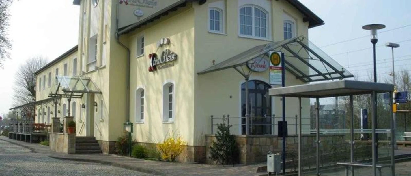 Bahnhof Hörstel Ehemaliger Bahnhof in Hellbeige und Weiß mit moderner Überdachung und Kopfsteinpflastervorplatz.