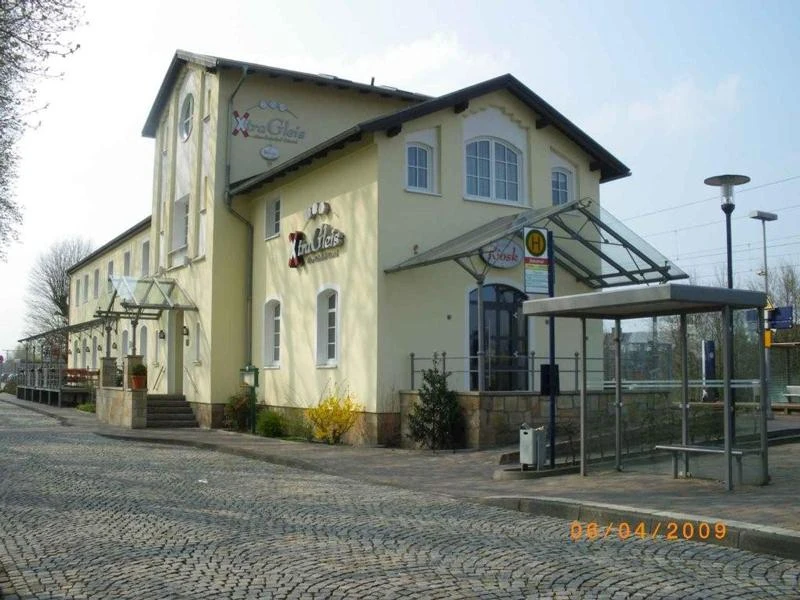 Bahnhof Hörstel Ehemaliger Bahnhof in Hellbeige und Weiß mit moderner Überdachung und Kopfsteinpflastervorplatz.
