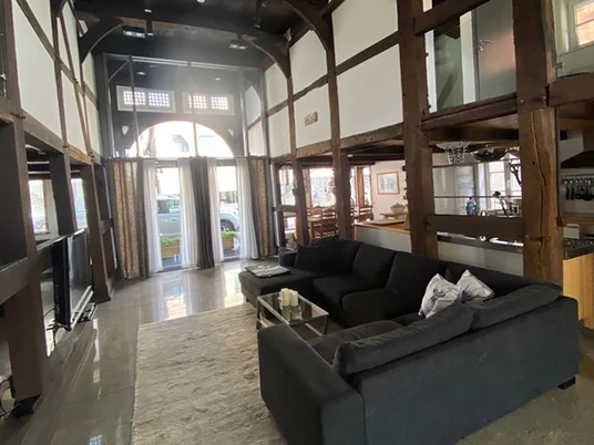 Wohnraum_komplett.jpg Offener Wohnbereich in einem Fachwerkhaus mit moderner Möblierung und großen, lichtdurchfluteten Fenstern.