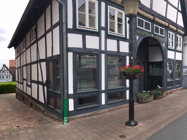Fachwerkhaus an einer gepflasterten Straße mit Blumenampel und klassischer schwarz-weißer Fassadengestaltung.