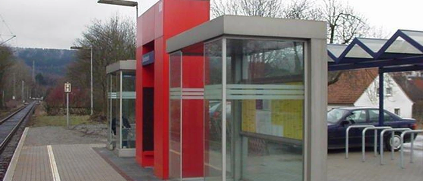 Bahnhof Sandebeck Moderner Bahnhof Sandebeck mit roten Schutzunterständen, Gleisen und umliegendem bewaldeten Hügel.