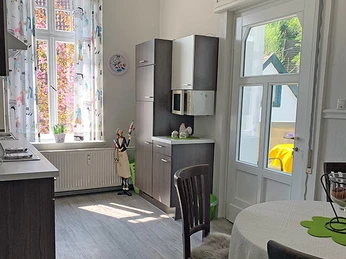 Küche Garden Apartment Helle Küche mit Esstisch und Stühlen, Holzschränken, großem Fenster und Glastür zum Garten.