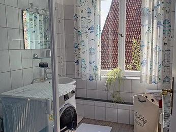 Badezimmer Apartment Garden Helles Badezimmer mit Dusche, Waschmaschine, weißen Fliesen und einem großen Fenster im Apartment Garden.