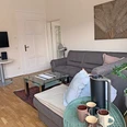 Wohnzimmer Apartment Gerome Helles Wohnzimmer mit grauem Sofa, Glastisch und Pflanzen. Moderne Einrichtung mit TV an der Wand.