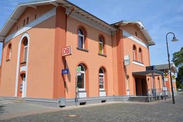 Bahnhof Marsberg Bahnhof Marsberg mit orangefarbener Fassade, Rundbogenfenstern und Bushaltestelle im Vordergrund.
