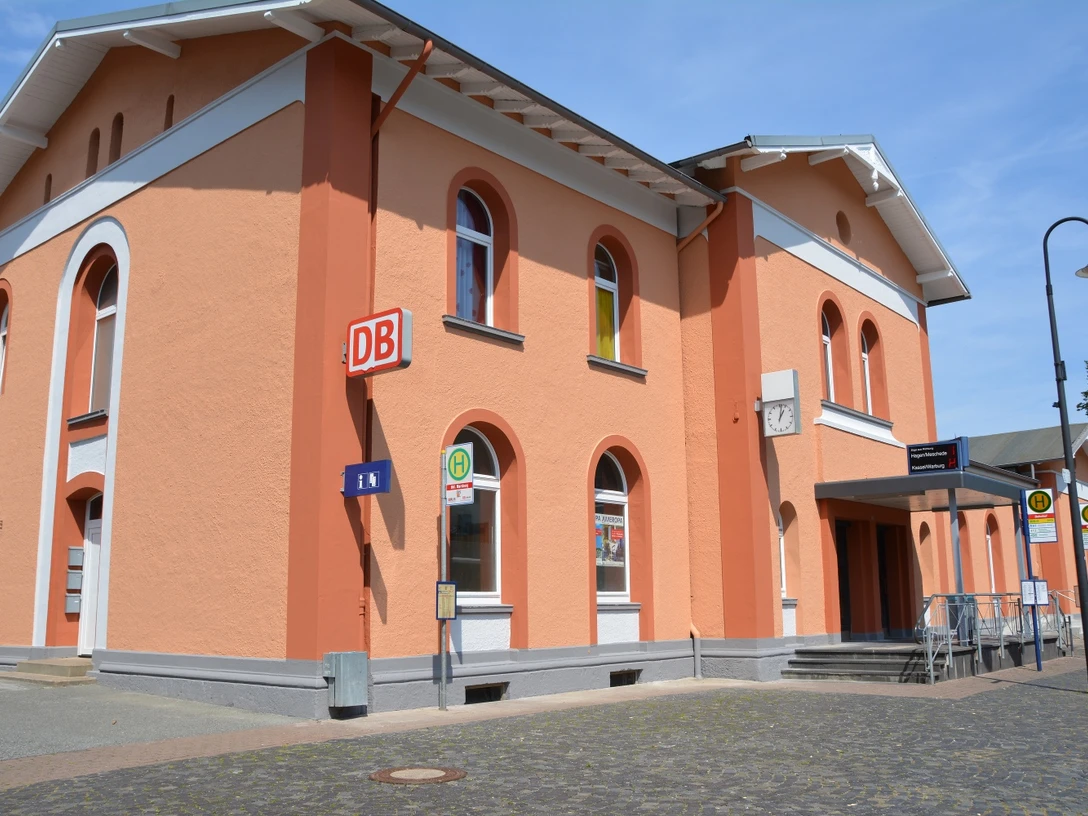 Bahnhof Marsberg Bahnhof Marsberg mit orangefarbener Fassade, Rundbogenfenstern und Bushaltestelle im Vordergrund.