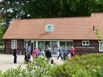 NaturZoo Rheine Menschen besuchen den Eingang des NaturZoos Rheine, umgeben von Bäumen und einem gepflasterten Weg.