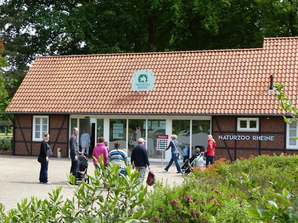 NaturZoo Rheine Menschen besuchen den Eingang des NaturZoos Rheine, umgeben von Bäumen und einem gepflasterten Weg.