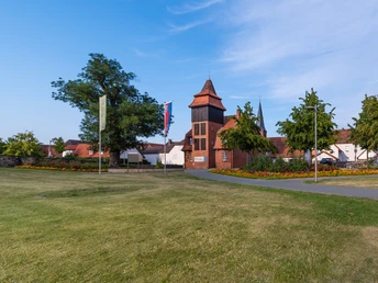 Historisches Gebäudeensemble mit einem zentralen, hohen Turm, umgeben von Rasen und blühenden Gärten.