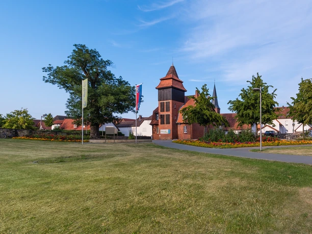 Historisches Gebäudeensemble mit einem zentralen, hohen Turm, umgeben von Rasen und blühenden Gärten.