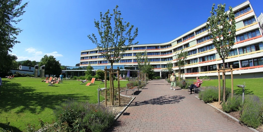 Knappschafts-Klinik Bad Driburg Moderner Klinikbau mit gepflegter Gartenanlage, Sonnenschirmen und Liegestühlen, klarer Himmel.