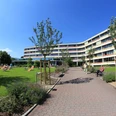 Knappschafts-Klinik Bad Driburg Moderner Klinikbau mit gepflegter Gartenanlage, Sonnenschirmen und Liegestühlen, klarer Himmel.