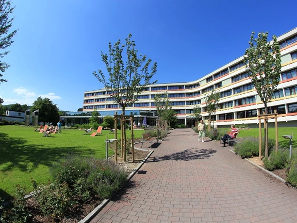 Knappschafts-Klinik Bad Driburg Moderner Klinikbau mit gepflegter Gartenanlage, Sonnenschirmen und Liegestühlen, klarer Himmel.
