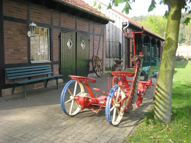 Landmaschinenmuseum Hörstel Rote, antike Pflugmaschine auf gepflastertem Hof vor einem Fachwerkgebäude mit grünen Türen.