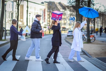 Science-Seeing-Tour durch Bielefeld.jpg Vier Menschen überqueren einen Zebrastreifen, zwei mit ungewöhnlichen Accessoires: Schachtel und Regenschirm.