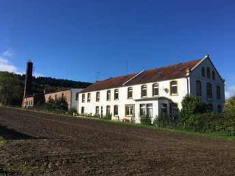 Ein zweistöckiges Landhaus mit rotem Dach neben einem Backsteingebäude in ländlicher Umgebung.