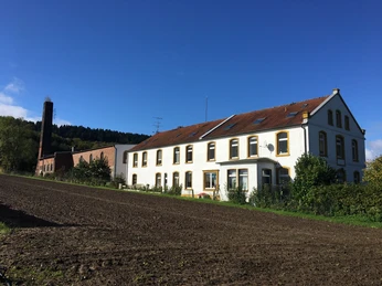 Ein zweistöckiges Landhaus mit rotem Dach neben einem Backsteingebäude in ländlicher Umgebung.