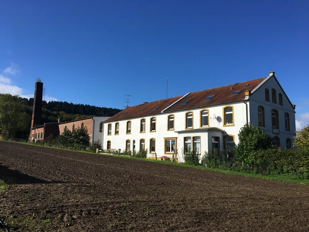 Ehemalige Knochenleimfabrik Ein zweistöckiges Landhaus mit rotem Dach neben einem Backsteingebäude in ländlicher Umgebung.