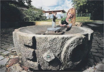 Ottilienquelle Paderborn (Archivbild) Steinbrunnen mit historischer Ornamentik, Frau betätigt den Wasserhahn, um frisches Quellwasser aufzufangen.