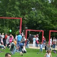 Schaukelparade im Flora-Westfalica-Park, Rheda-Wiedenbrück Menschen im Park genießen ein sonniges Fest mit roten Rahmen-Schaukeln, umgeben von Bäumen.