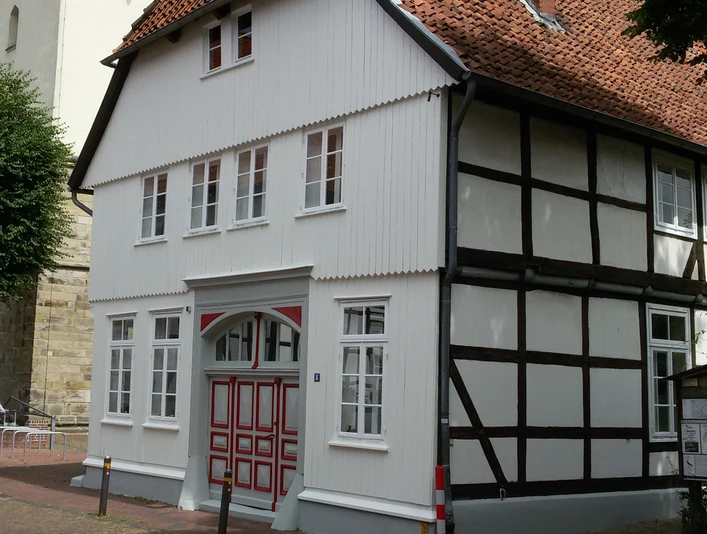 Fachwerkhaus mit rotem Ziegeldach und weißen Fenstern, teils verschattet unter blauem Himmel.