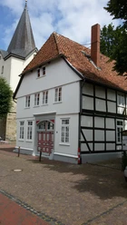 Storchenhaus in NRÜ Außenansicht Fachwerkhaus mit rotem Ziegeldach und weißen Fenstern, teils verschattet unter blauem Himmel.