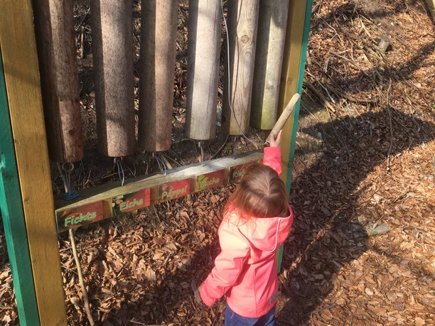 Mädchen spielt auf einem Außenspielgerät namens Dendrophon aus Baumstämmen im Herbstwald.