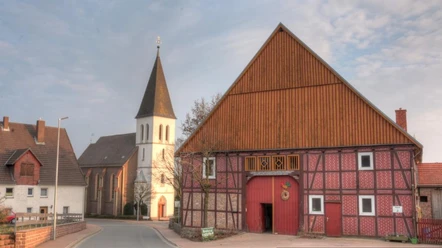Haarbrück Eine historische Fachwerkscheune in Haarbrück mit einem Kirchturm im Hintergrund bei bewölktem Himmel.