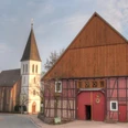 Haarbrück Eine historische Fachwerkscheune in Haarbrück mit einem Kirchturm im Hintergrund bei bewölktem Himmel.