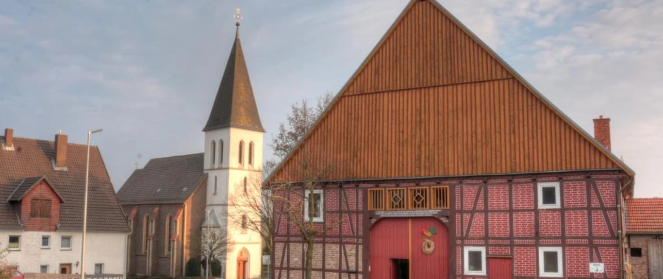 Haarbrück Eine historische Fachwerkscheune in Haarbrück mit einem Kirchturm im Hintergrund bei bewölktem Himmel.