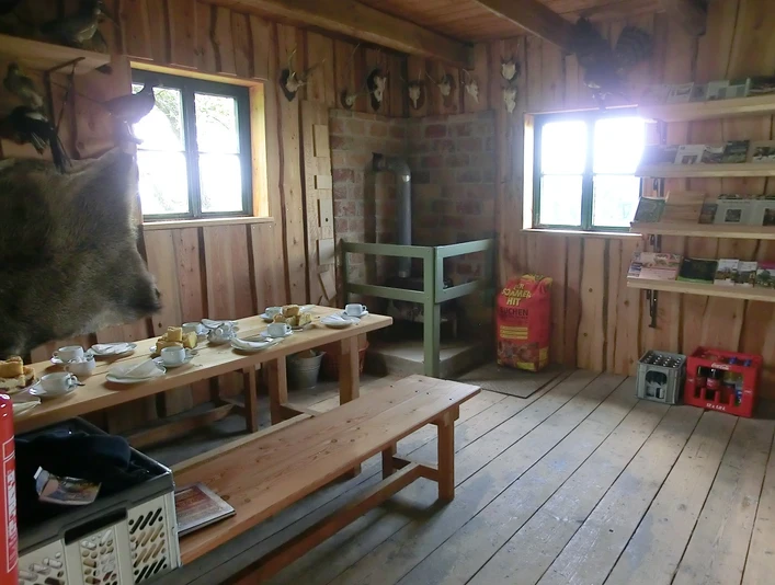 Räumlichkeiten in der Waldschule Modexen Rustikale Holzausstattung in einem Raum mit Sitzbänken, gedecktem Tisch und dekorativen Jagdtrophäen.