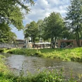Wiehlpark Grüne Parklandschaft mit Fluss, Brücke, Bäumen und Menschen unter Pavillons an einem sonnigen Tag.