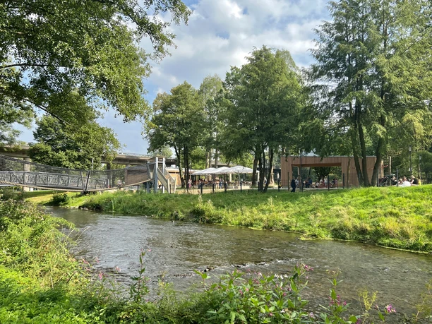 Wiehlpark Grüne Parklandschaft mit Fluss, Brücke, Bäumen und Menschen unter Pavillons an einem sonnigen Tag.