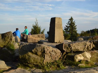 Lippische Velmerstot in der Abendstimmung Zwei Personen sitzen im Licht der untergehenden Sonne auf Felsen, mit Ausblick auf Wälder.