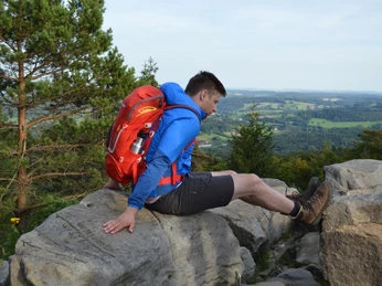 Ausblick vom Felsen Richtung Steinheim Ein Wanderer mit rotem Rucksack sitzt auf einem Felsen, blickt über hügelige Waldlandschaft.