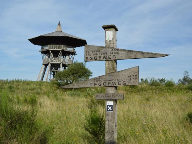 Eggeturm aus Holz auf einer Wiese; Wegweiser Richtung Eggeweg und Preußische Velmerstot im Vordergrund.