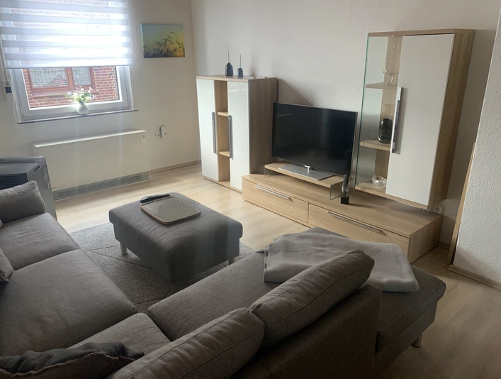 Wohnzimmer Modernes Wohnzimmer mit grauem Sofa, Couchtisch, Flachbildfernseher und hellem Holzschränken.