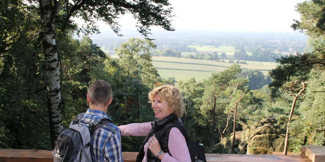 Blick von der Aussichtsplattform an der Almhütte Zwei Wanderer genießen den weiten Blick über Wälder und Felder von einer hölzernen Plattform.