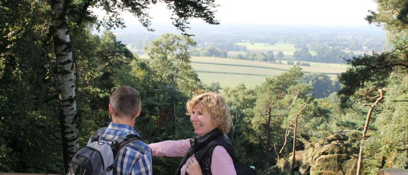 Blick von der Aussichtsplattform an der Almhütte Zwei Wanderer genießen den weiten Blick über Wälder und Felder von einer hölzernen Plattform.