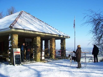 Winterliche Schwedenschanze mit schneebedecktem Dach, Besuchern und Blick auf die verschneite Landschaft.